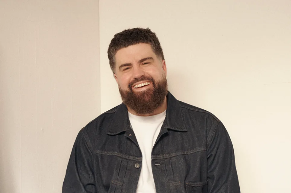 James Hazlett-Beard laughing, in a denim jacket against a plain wall